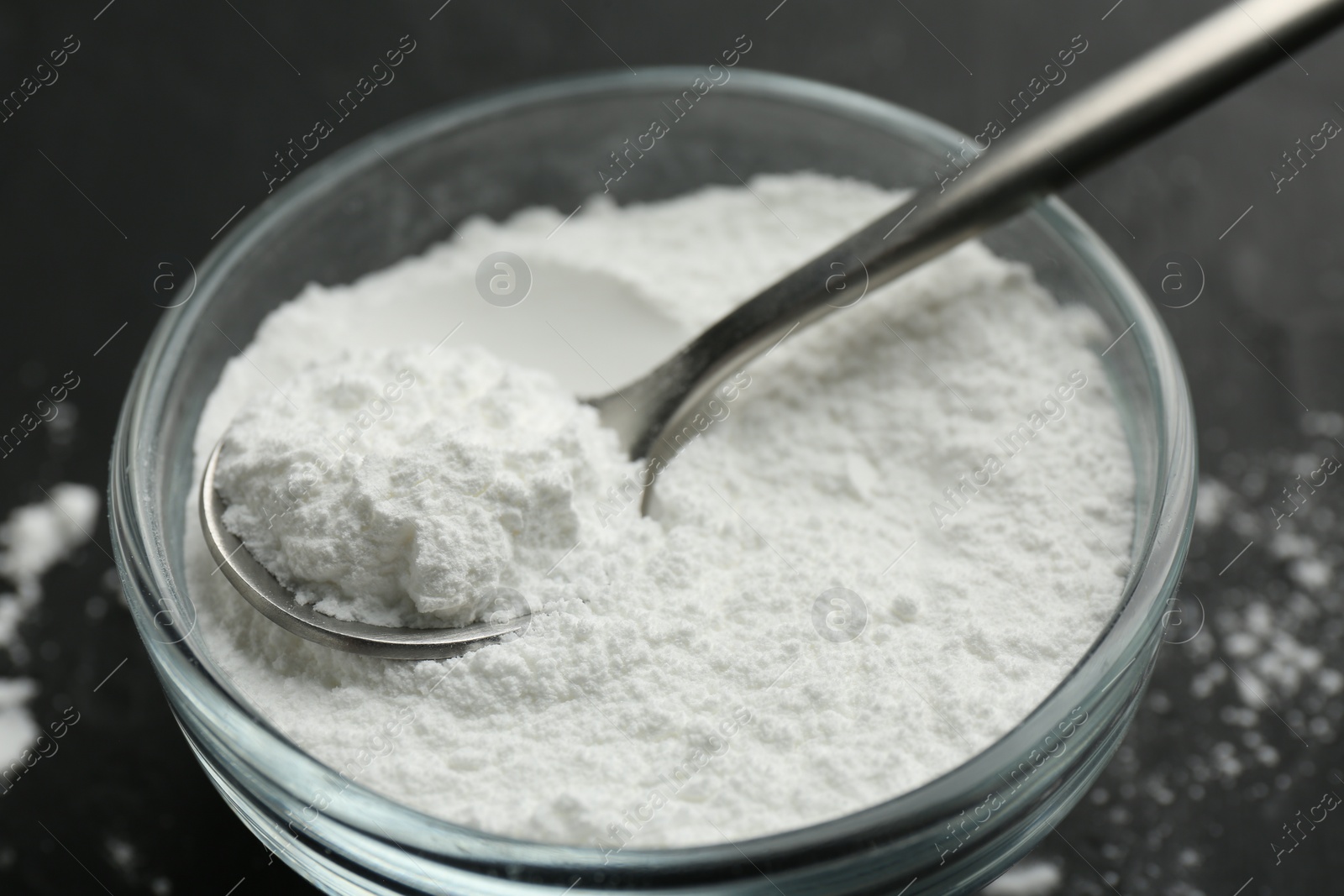 Photo of Baking powder in bowl and spoon on black table, closeup