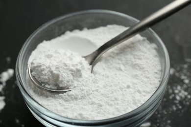 Baking powder in bowl and spoon on black table, closeup