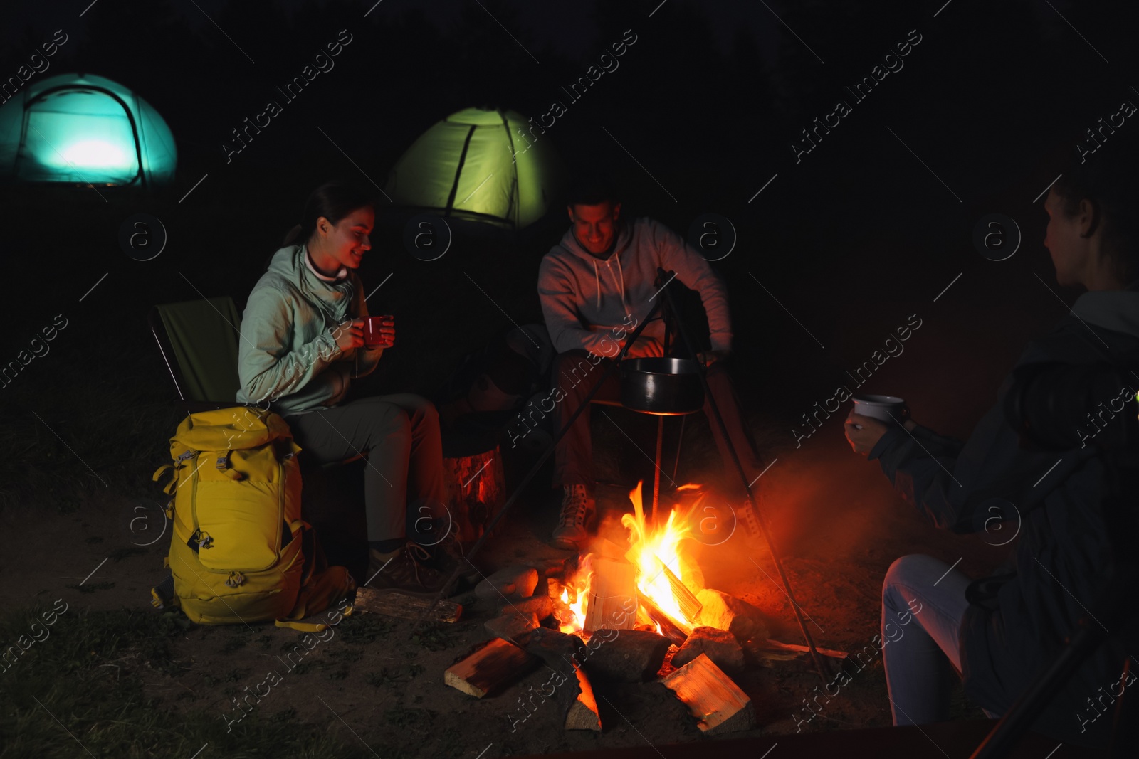 Photo of Friends sitting around bonfire outdoors in evening. Camping season