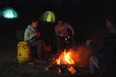 Photo of Friends sitting around bonfire outdoors in evening. Camping season