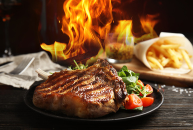 Image of Tasty beef steak and flame on black wooden table