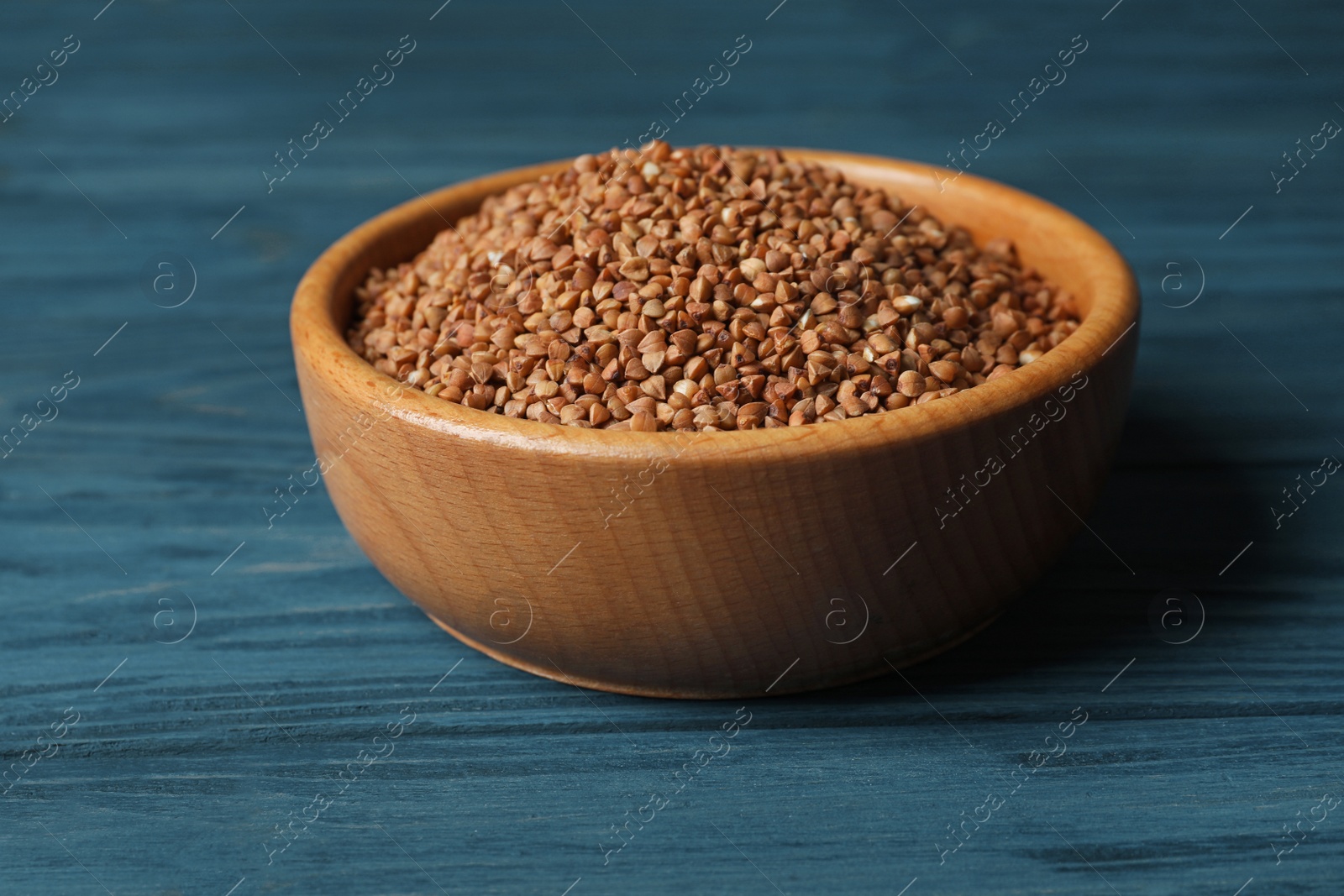 Photo of Uncooked buckwheat in bowl on wooden table