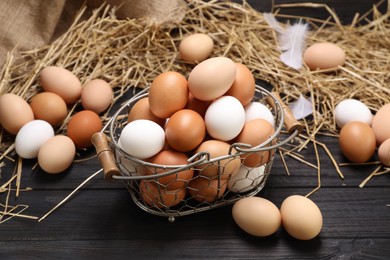 Photo of Fresh chicken eggs and dried straw on black wooden table