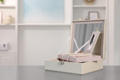 Photo of Jewelry box with mirror and many accessories on grey table indoors. Space for text