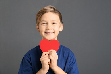 Photo of Cute boy with paper heart on grey background. Space for text