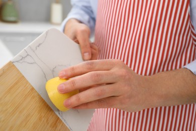 Photo of Man rubbing cutting board with lemon at home, closeup