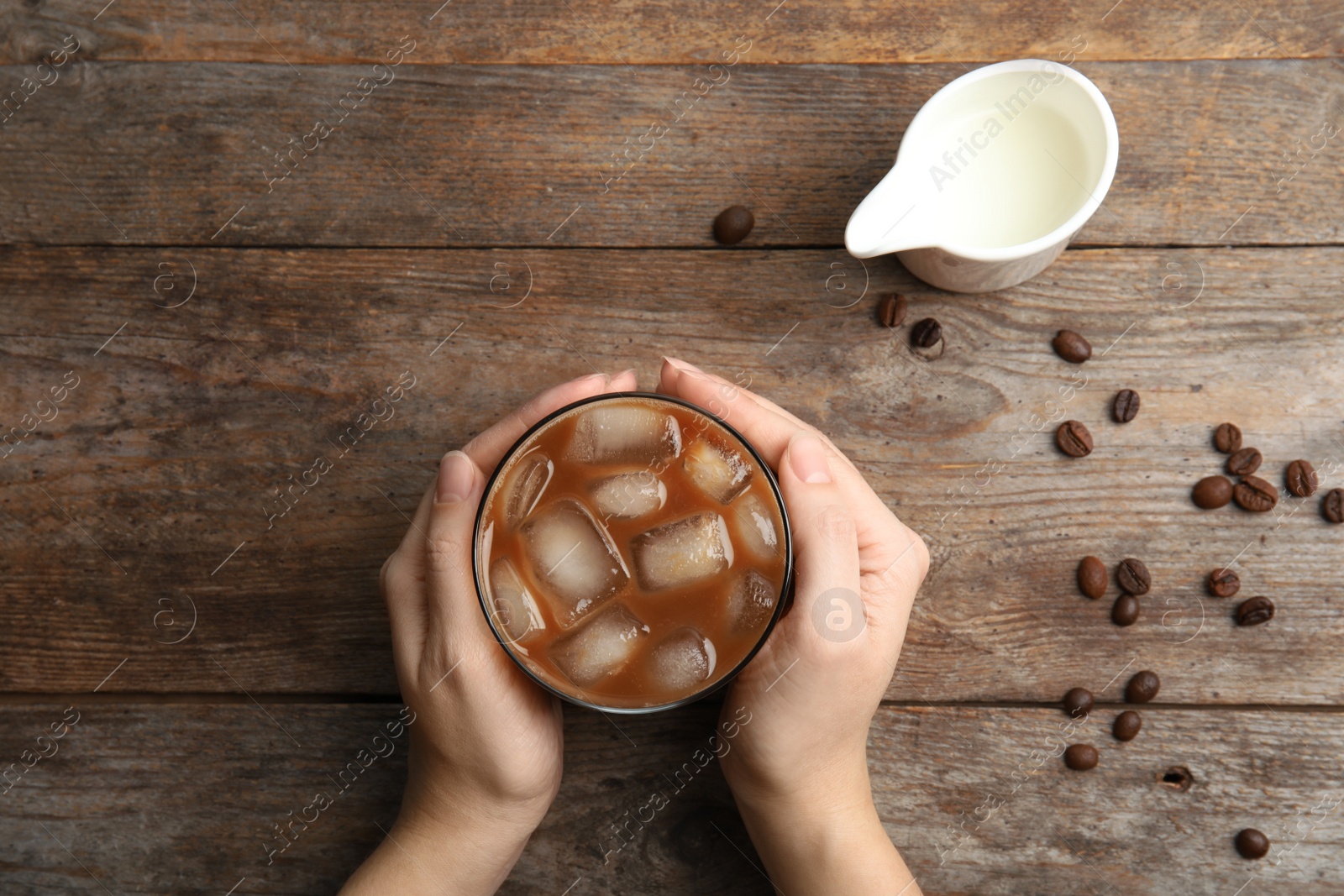 Photo of Woman holding glass of coffee with ice cubes at table, top view