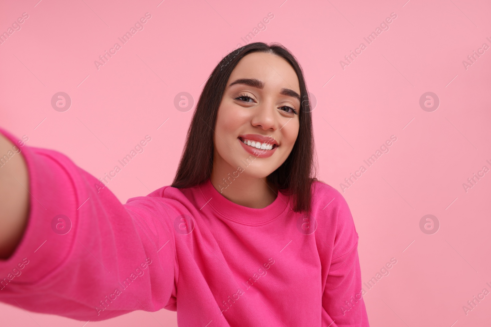 Photo of Smiling young woman taking selfie on pink background