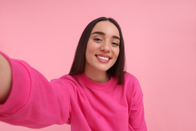 Smiling young woman taking selfie on pink background