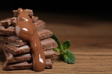 Photo of Pieces of milk chocolate with tasty paste and mint on wooden table, closeup. Space for text