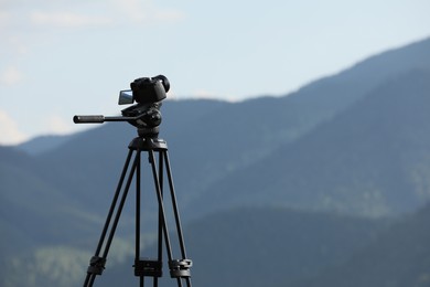 Photo of Tripod with modern camera in mountains. Space for text