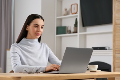 Photo of Woman working with laptop at wooden desk in room