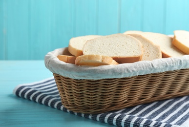 Photo of Slices of tasty fresh bread in wicker basket on light blue wooden table, closeup