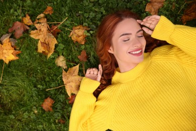 Photo of Smiling woman lying on grass among autumn leaves, top view. Space for text