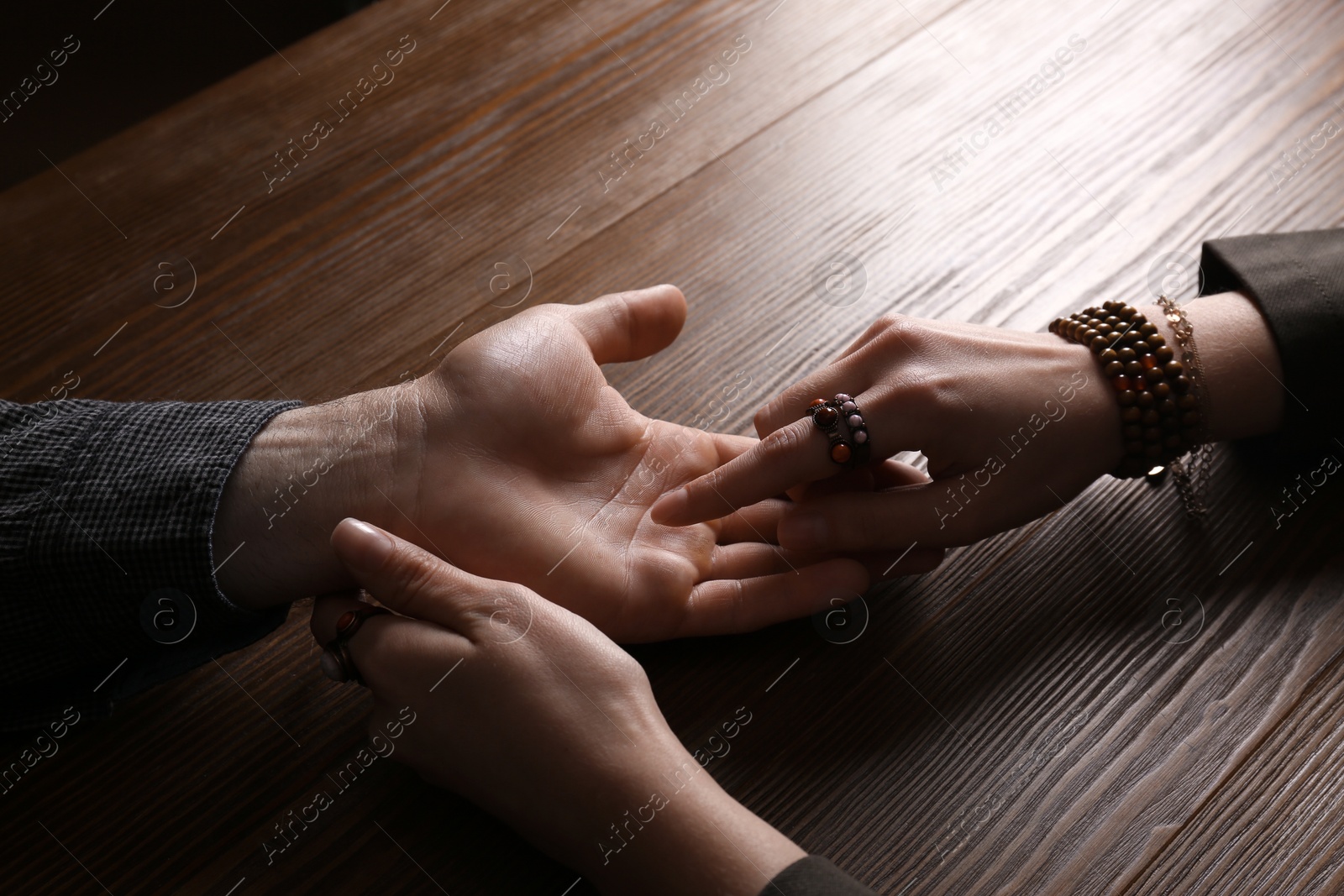 Photo of Chiromancer reading lines on man's palm at table, closeup