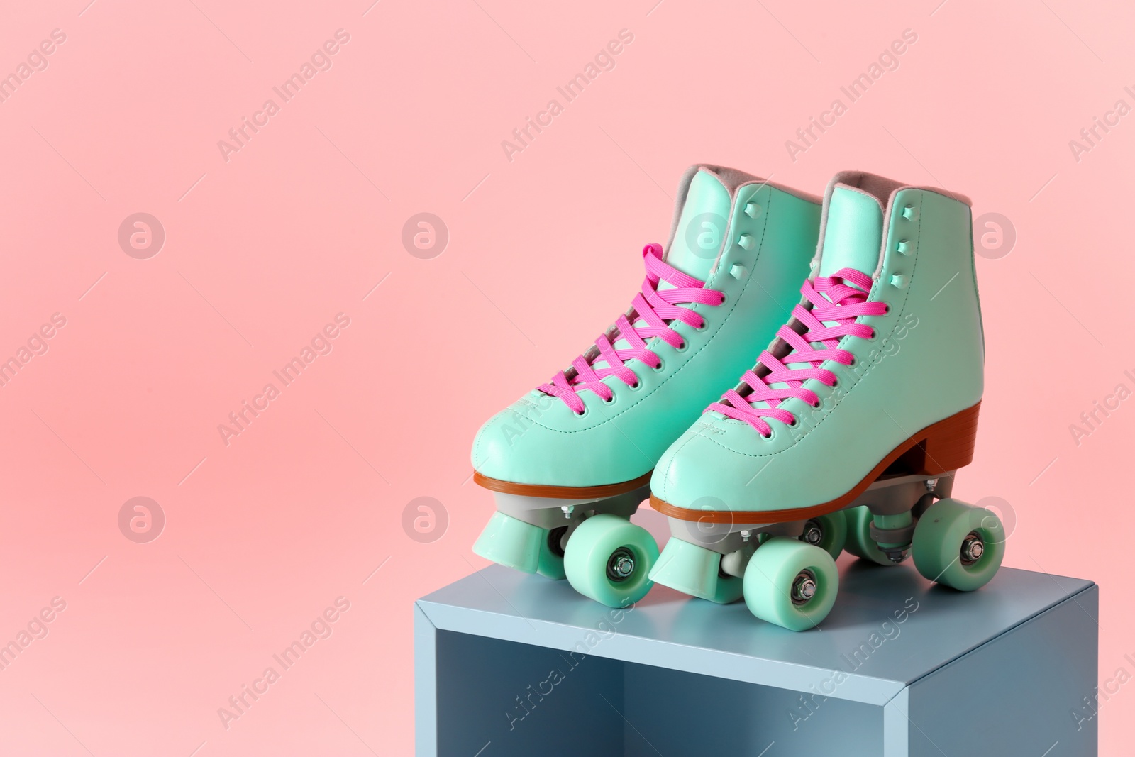 Photo of Pair of vintage roller skates on storage cube against color background. Space for text