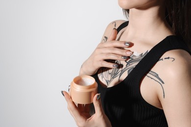 Woman applying healing cream onto her tattoos against light background, closeup. Space for text