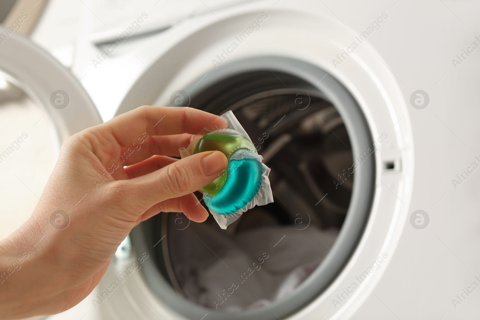 Photo of Woman holding laundry detergent capsule near washing machine, closeup