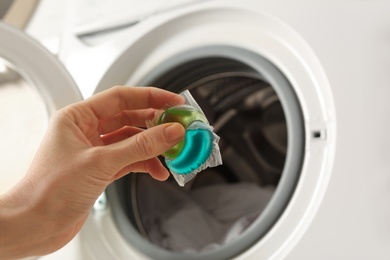 Photo of Woman holding laundry detergent capsule near washing machine, closeup