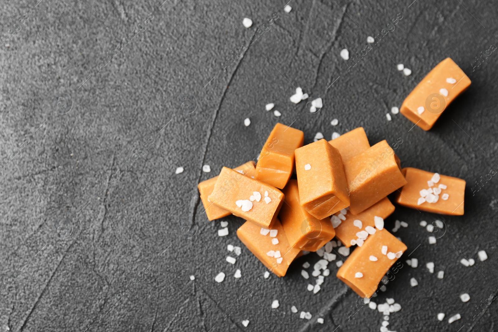 Photo of Delicious caramel candies with salt on dark background, top view