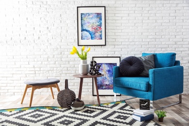 Photo of Modern living room interior with comfortable armchair and stool near brick wall