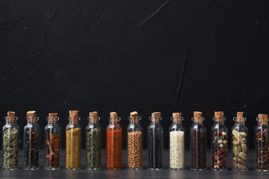 Photo of Glass bottles with different spices on table against black background