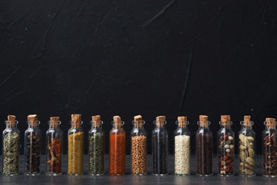 Glass bottles with different spices on table against black background