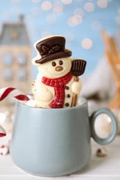 Photo of Funny chocolate snowman candy in cup of hot drink on white table