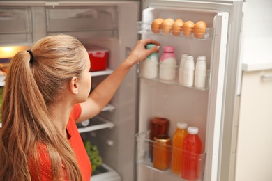 Photo of Young woman taking yogurt from refrigerator at home