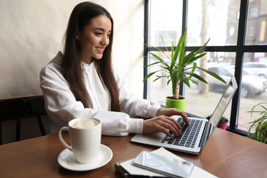 Photo of Young blogger working with laptop in cafe