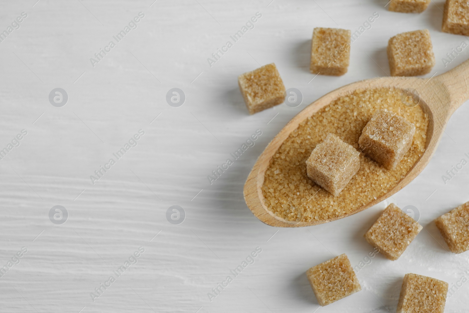 Photo of Brown sugar cubes in spoon on white wooden table, closeup. Space for text