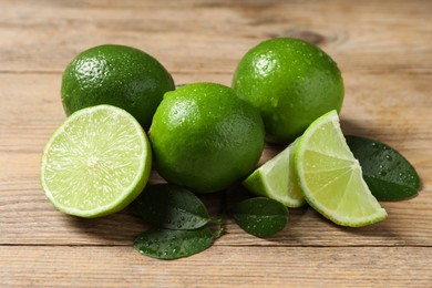 Photo of Fresh ripe limes and green leaves with water drops on wooden table