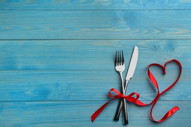 Photo of Cutlery set with red ribbon and space for text on light blue wooden background, flat lay. Valentine's Day dinner