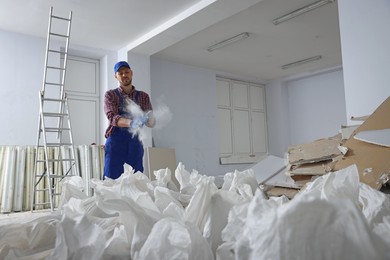 Construction worker shaking off dust from hands in room prepared for renovation