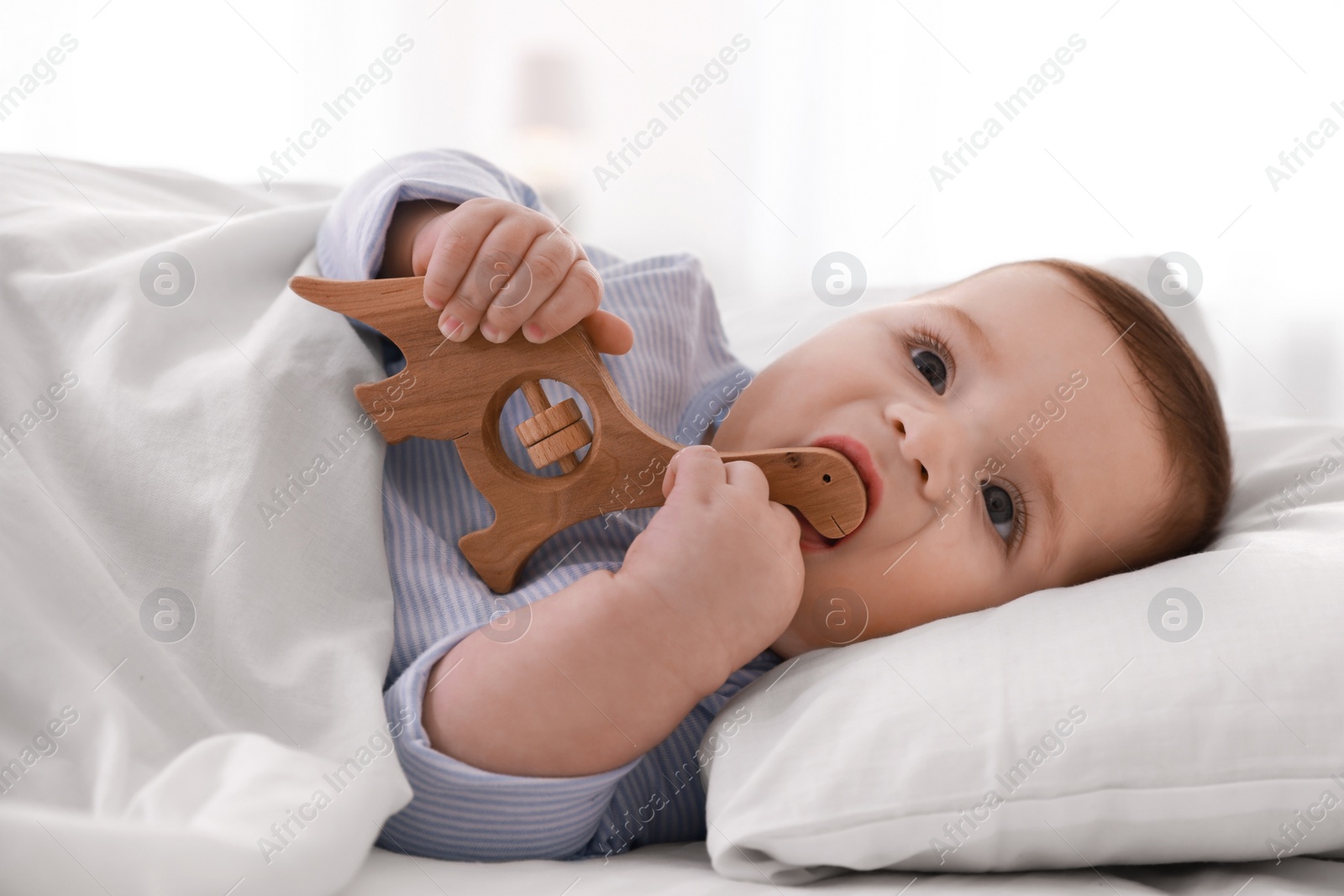 Photo of Cute little baby with toy lying in bed under soft blanket indoors