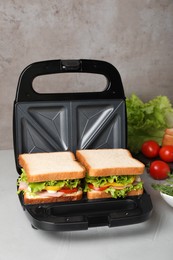 Photo of Modern grill maker with tasty sandwiches on light grey table