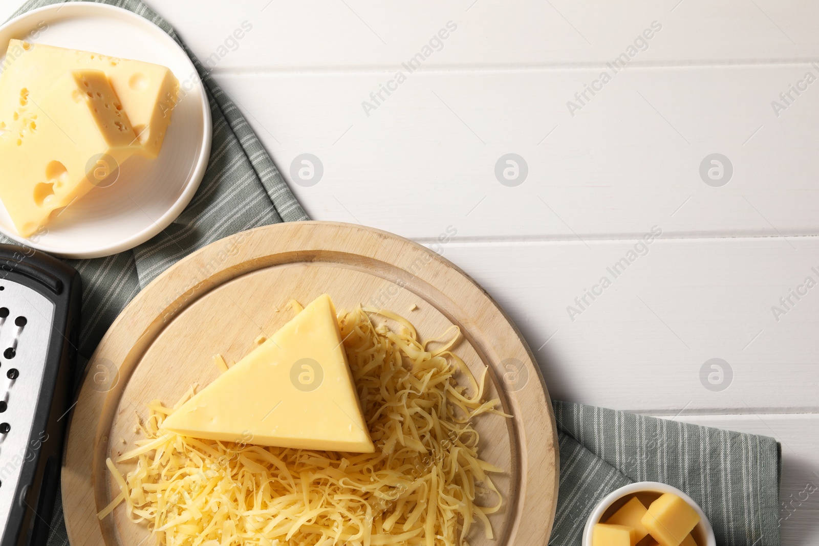 Photo of Grated and whole pieces of cheese on white wooden table, flat lay. Space for text