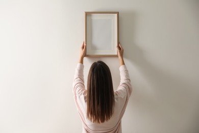 Photo of Woman hanging picture on white wall indoors