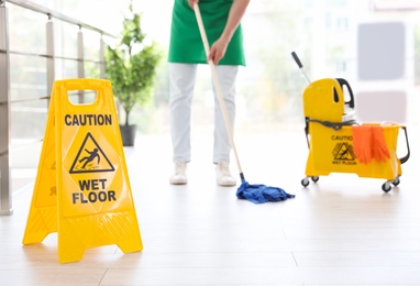 Safety sign with phrase "CAUTION WET FLOOR" and young man on background