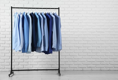 Photo of Dry-cleaning service. Many different clothes hanging on rack near white brick wall, space for text