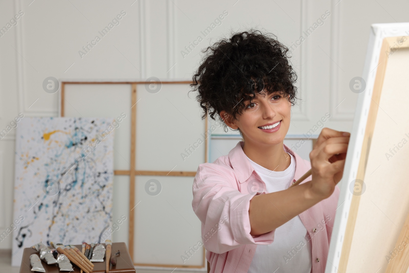 Photo of Young woman painting on easel with canvas in studio