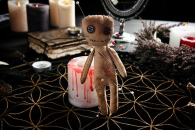 Photo of Voodoo doll pierced with pins near candle on table indoors. Curse ceremony