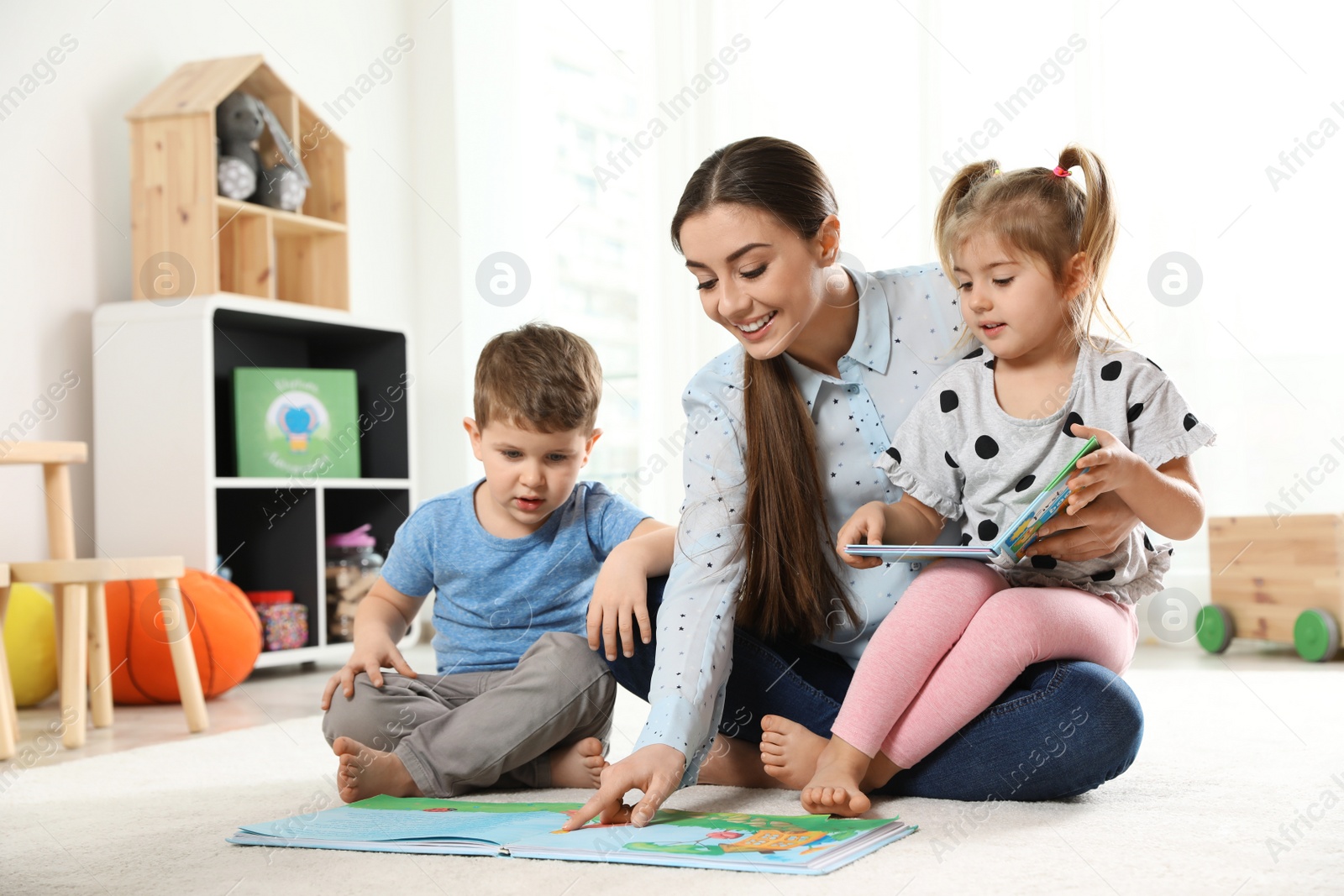 Photo of Kindergarten teacher reading book to children indoors. Learning and playing