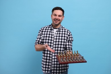 Photo of Smiling man showing chessboard with game pieces on light blue background