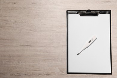 Photo of Clipboard and thermometer on wooden table, top view. Space for text