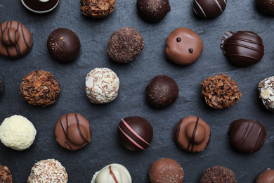 Photo of Different delicious chocolate candies on black table, flat lay