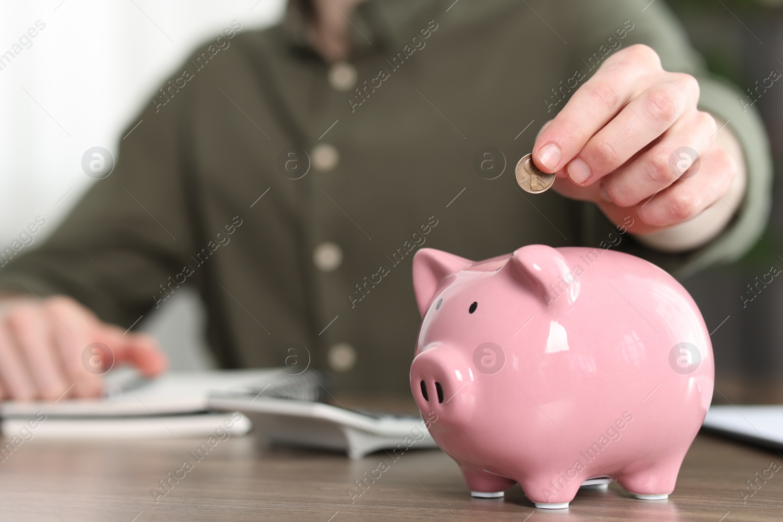 Photo of Financial savings. Man putting coin into piggy bank at wooden table, closeup