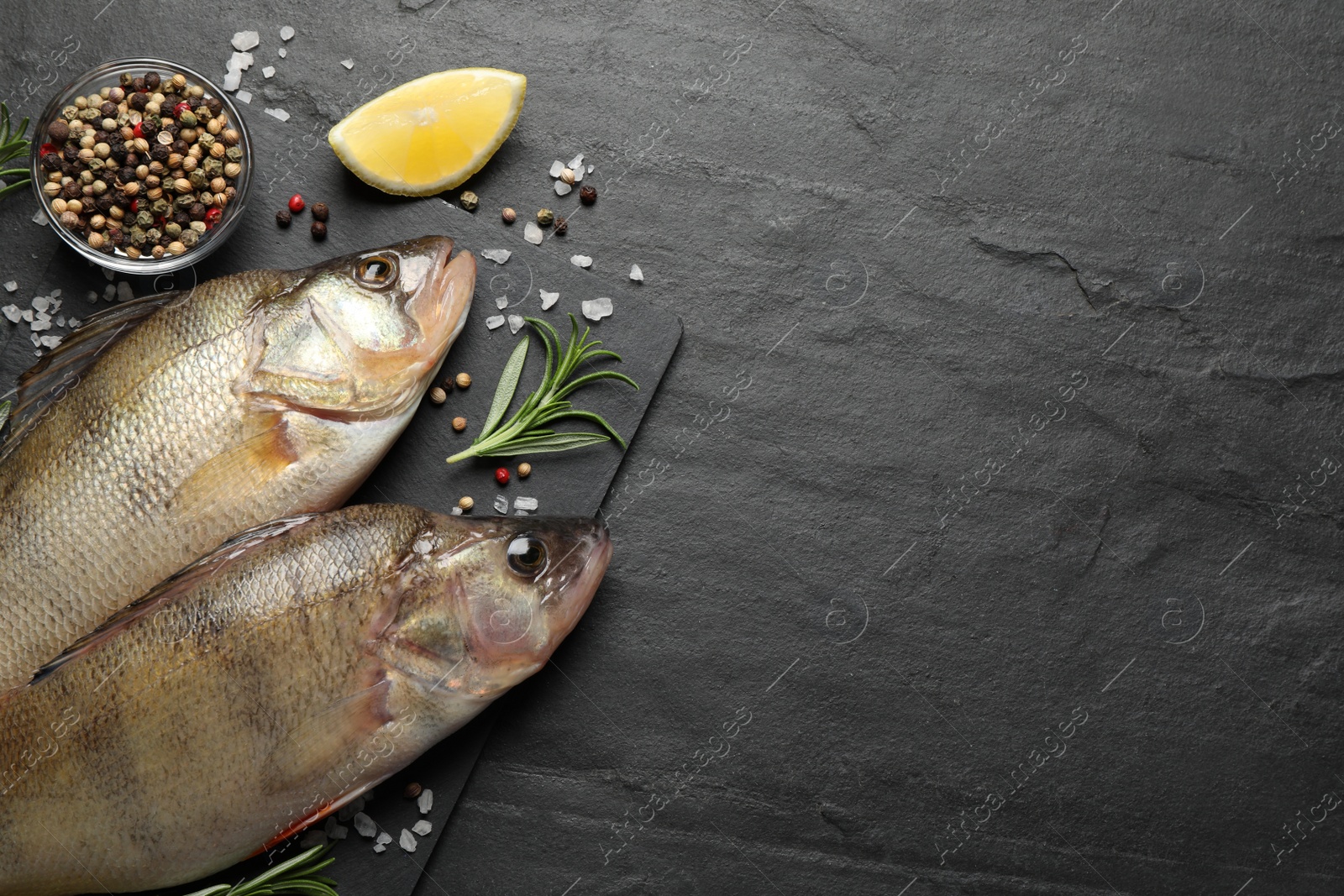 Photo of Fresh raw perches and ingredients on black slate table, flat lay with space for text. River fish