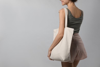 Back view of happy young woman with blank eco friendly bag on light background, closeup. Space for text