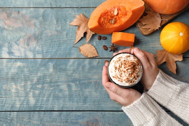 Photo of Woman holding glass cup of tasty pumpkin spice latte on wooden table, flat lay with space for text